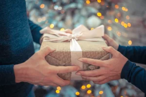 In the picture, a close-up on the hands of two persons swapping a gift.